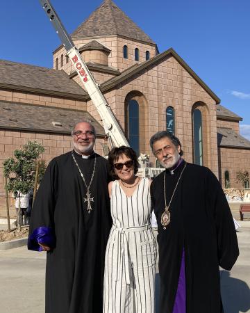 Photo of Beth in front of the new church building with two priests.