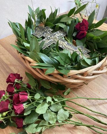 Image of an Orthodox Cross in a basket surrounded by bay leaves, olive leaves, and roses before being placed in Church for veneration